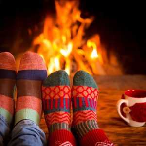 socked feet on coffee table with mug in front of fireplace